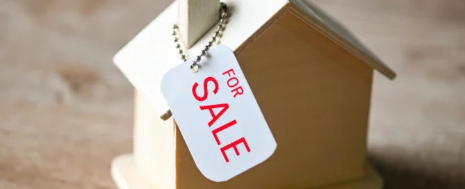 Wooden house model with 'For Sale' tag attached, representing property for sale.