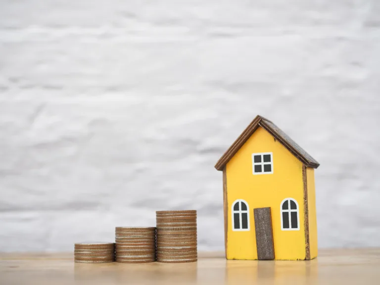 Miniature yellow house next to stacks of coins, symbolising property value and costs of selling a home.