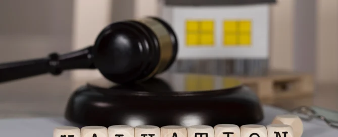 The image shows wooden blocks spelling out the word "VALUATION" placed in front of a small house model and a gavel, symbolising property valuation and legal considerations.