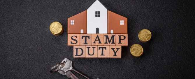 Stamp duty concept with a house model, wooden letter blocks spelling 'STAMP DUTY,' British pound coins, and house keys on a dark background.