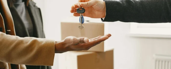Professional estate agent handing over house keys to new homeowner with moving boxes in background