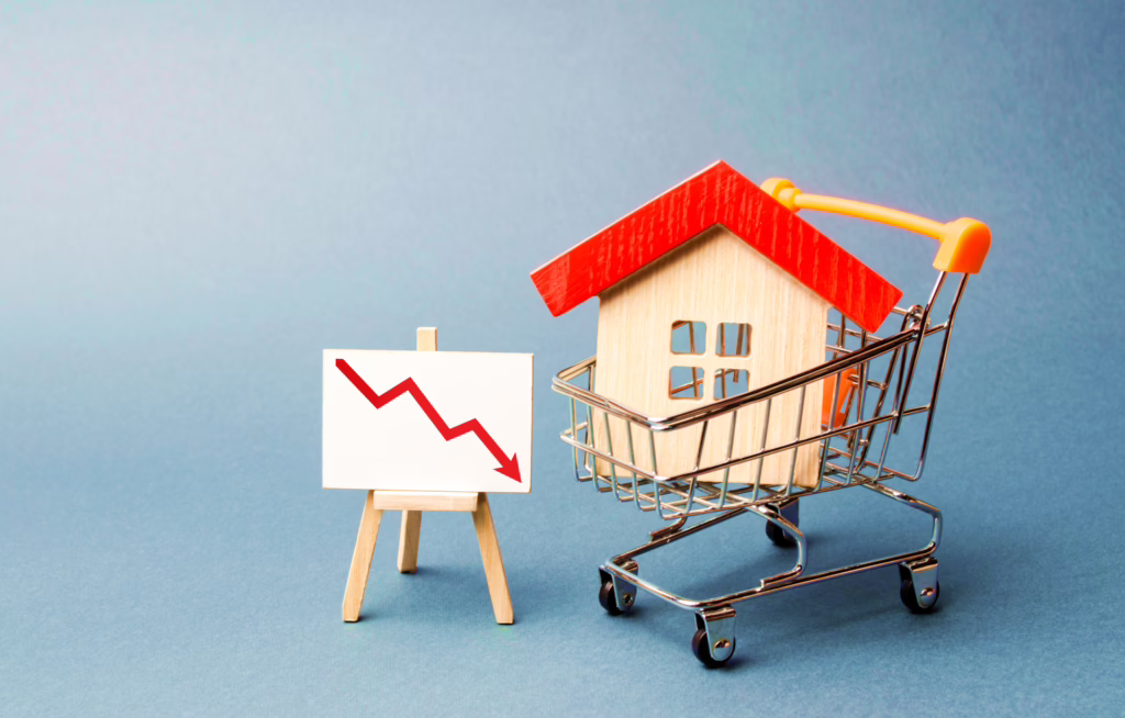 Image showing a wooden house in a shopping cart next to a red trend line chart, representing changes in the housing market.