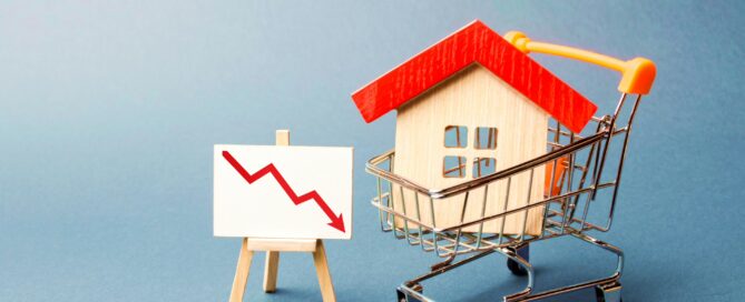 Image showing a wooden house in a shopping cart next to a red trend line chart, representing changes in the housing market.