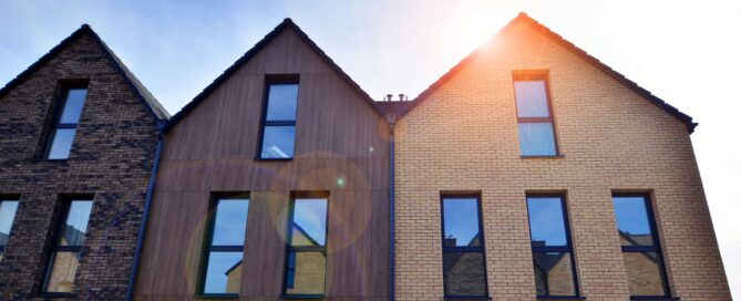Modern row of newly built homes with brick and wood facades under bright sunlight.