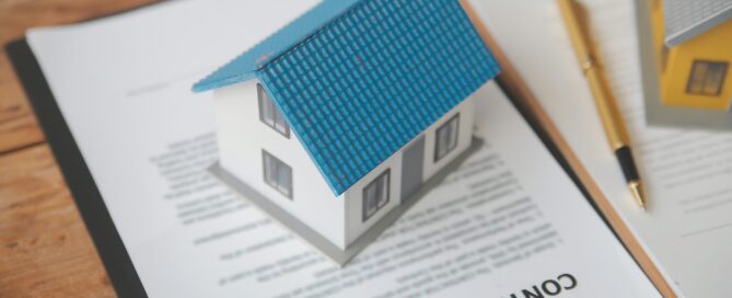 Model house placed on top of a contract agreement with a pen nearby, representing real estate paperwork and property transactions.
