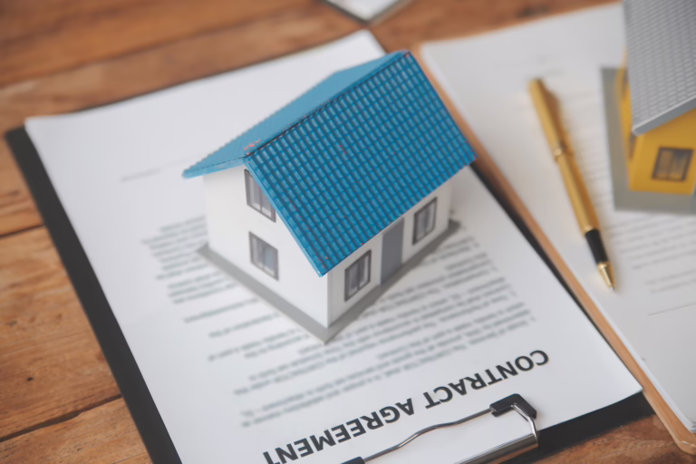 Model house placed on top of a contract agreement with a pen nearby, representing real estate paperwork and property transactions.