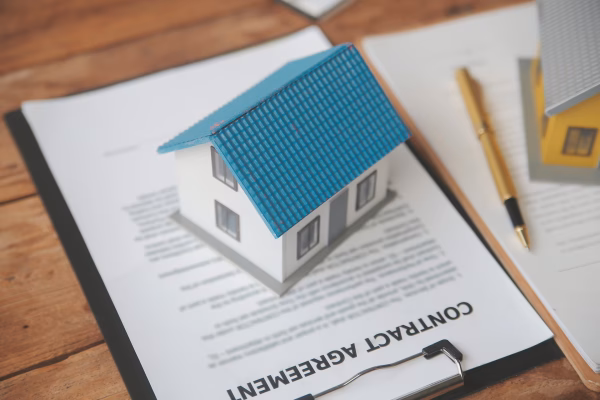 Model house placed on top of a contract agreement with a pen nearby, representing real estate paperwork and property transactions.