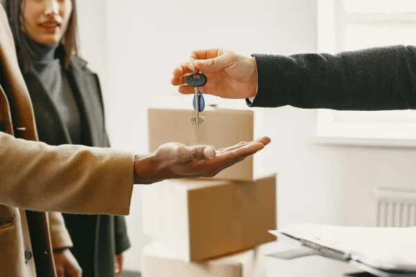 Professional estate agent handing over house keys to new homeowner with moving boxes in background