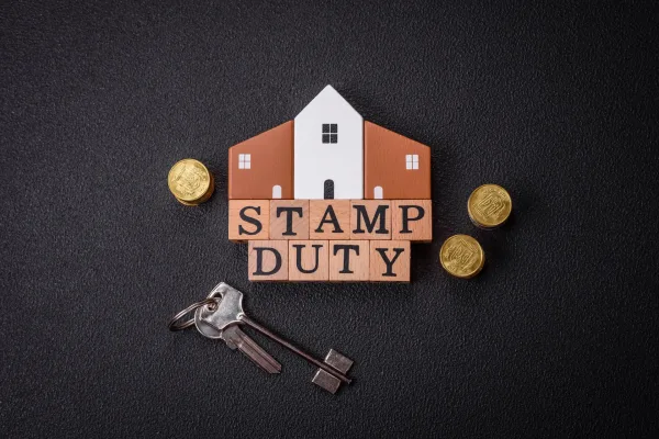 Stamp duty concept with a house model, wooden letter blocks spelling 'STAMP DUTY,' British pound coins, and house keys on a dark background.